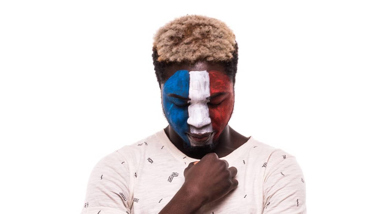 Un homme au visage peint aux couleurs du drapeau français baisse la tête, symbolisant une réflexion profonde ou un sentiment de résilience.