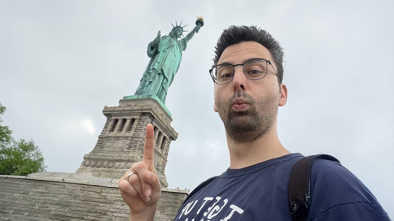 Portrait de l'auteur (Arnaud Baudet) debout face à la Statue de la Liberté, symbole de flamme intérieure retrouvée et de liberté créative.