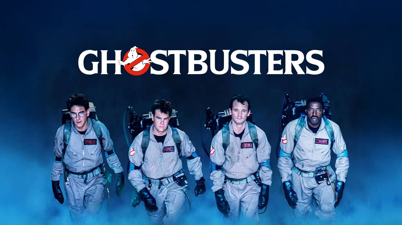 Image promotionnelle du film Ghostbusters, montrant les quatre chasseurs de fantômes emblématiques en combinaison beige, équipés de packs à protons, avançant dans un nuage de fumée bleutée, avec le logo Ghostbusters en haut de l’image.