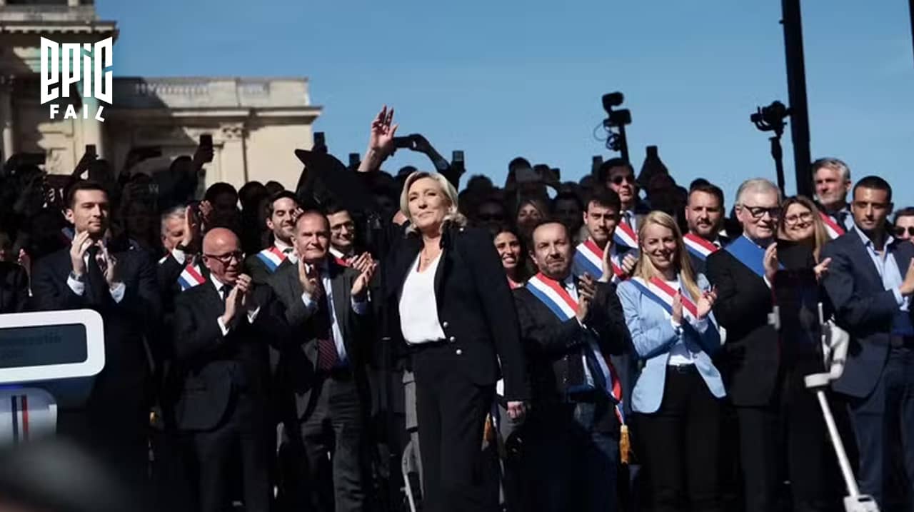 Marine Le Pen saluant ses partisans lors d’un rassemblement à Paris, entourée d’élus du Rassemblement national applaudissant, sous un ciel bleu.